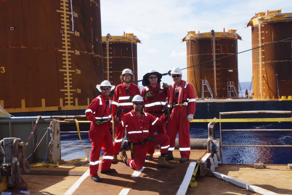 A group of offshore workers in red jumpsuits are smiling at the camera